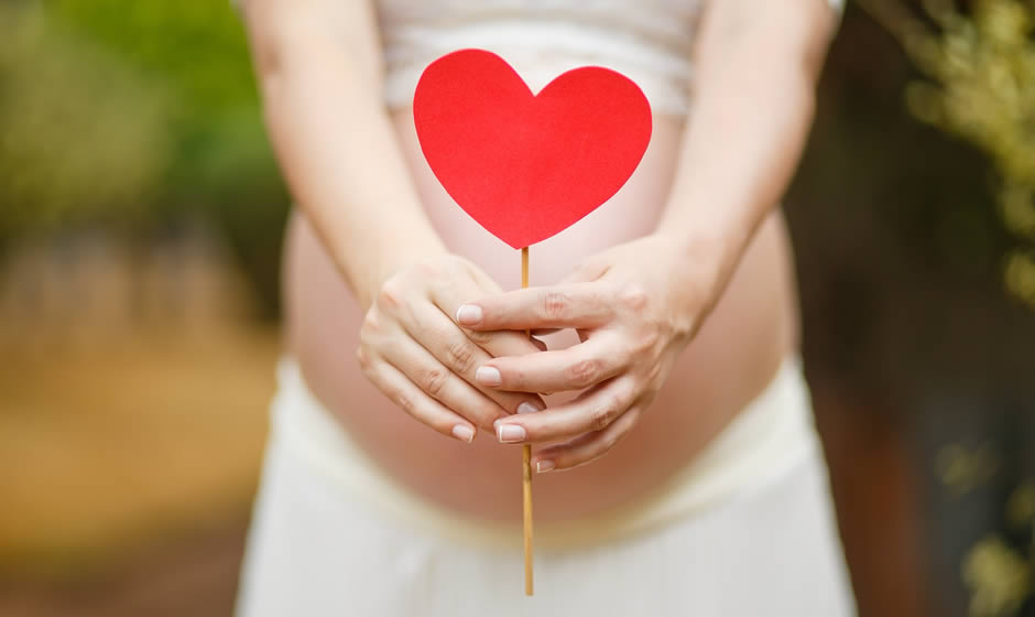 Donna in gravidanza con un cuoricino fra le mani