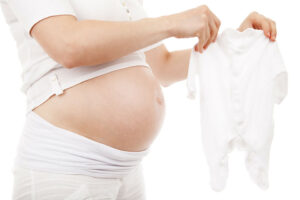 Donna in gravidanza con tutina neonato in mano